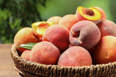 Photo of Cut and whole fresh ripe peaches in basket on wooden table against blurred background, closeup. Space for text