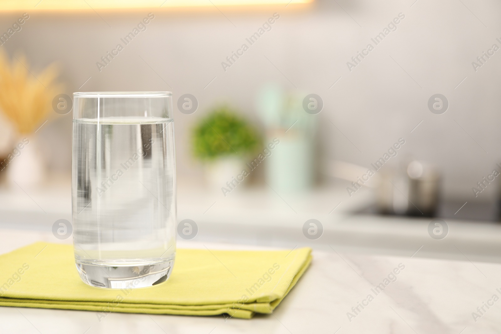 Photo of Glass with clear water on white marble table in kitchen, space for text