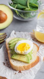 Photo of Delicious sandwich with boiled egg and pieces of avocado on gray table