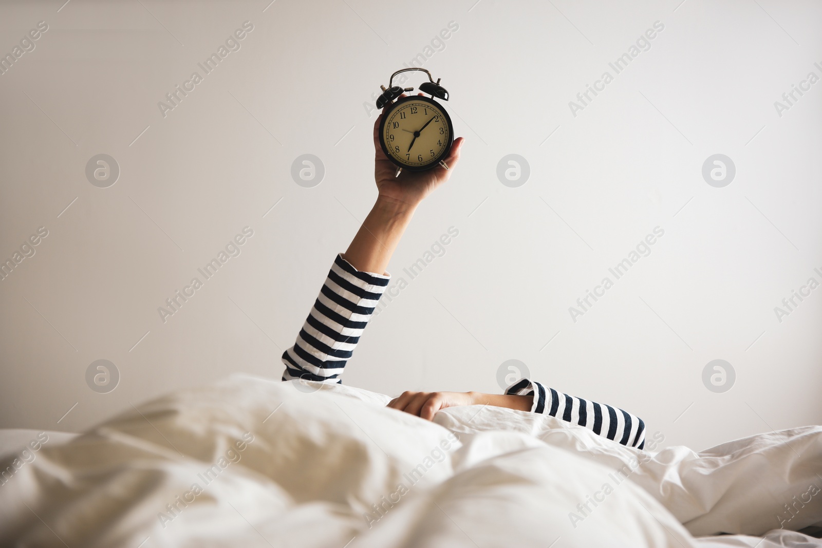 Photo of Woman with alarm clock lying in bed, closeup. Morning time
