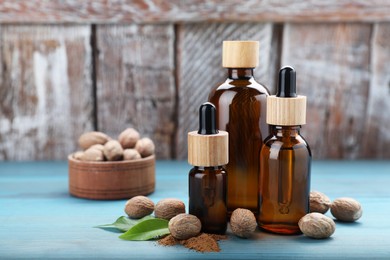 Bottles of nutmeg oil, nuts and powder on turquoise wooden table. Space for text