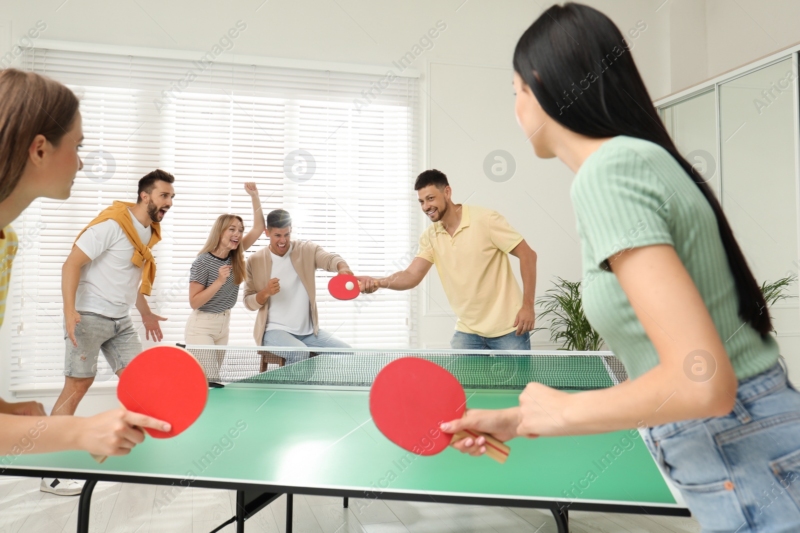 Photo of Happy friends playing ping pong together indoors