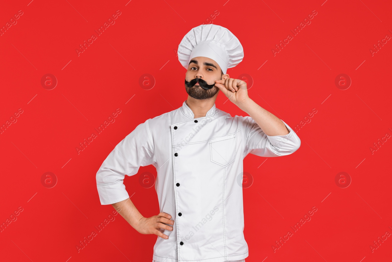 Photo of Professional chef with funny artificial moustache on red background