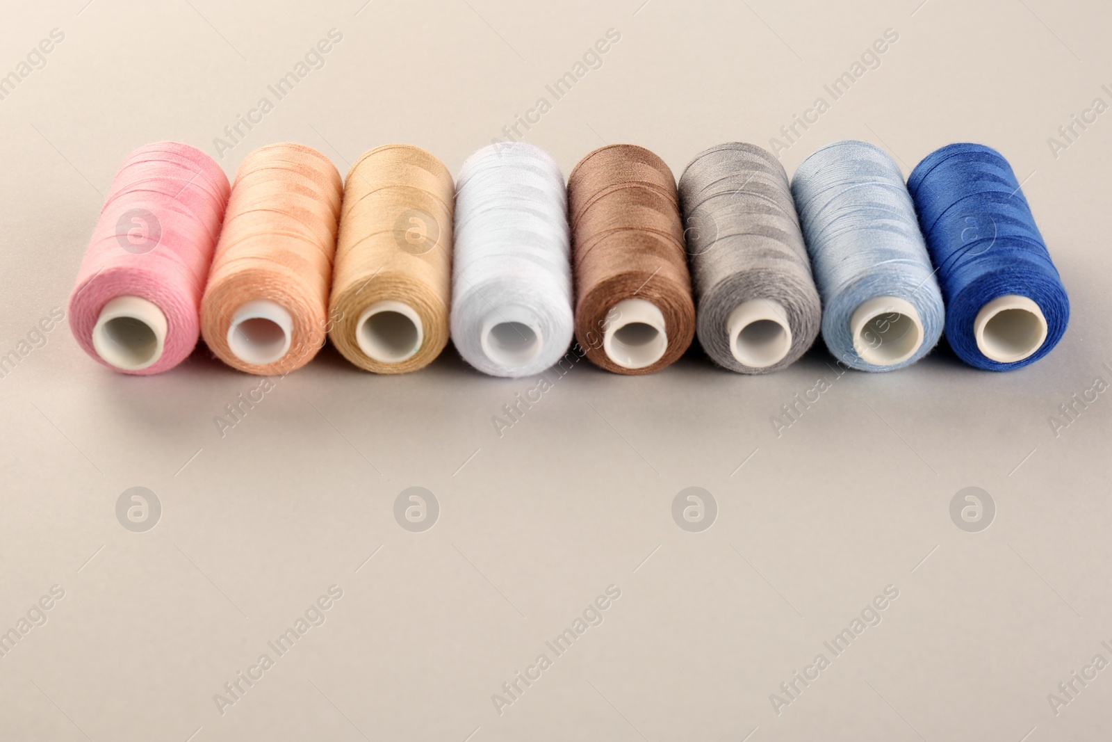 Photo of Different sewing threads on light grey background. Space for text