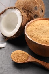 Photo of Spoon with coconut sugar, bowl and fruits on dark textured table, closeup