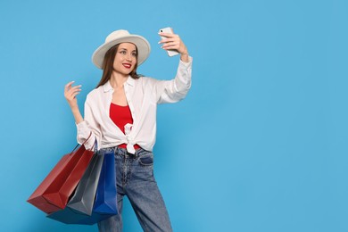 Photo of Stylish young woman with shopping bags taking selfie on light blue background, space for text