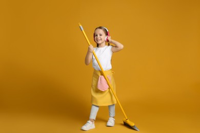 Photo of Cute little girl in headphones with broom on orange background
