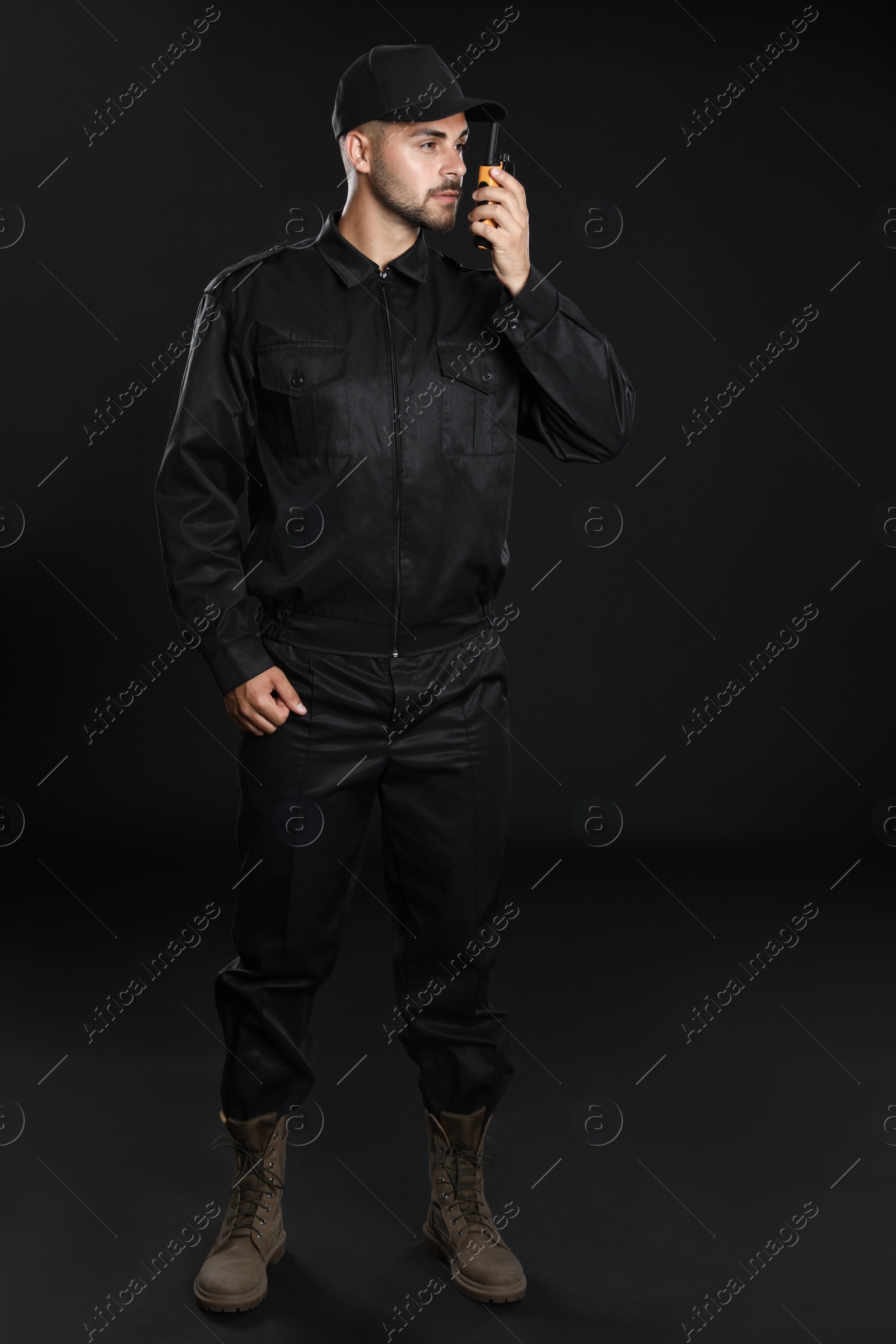 Photo of Male security guard in uniform using portable radio transmitter on dark background