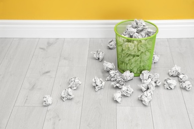 Photo of Metal bin with crumpled paper on floor near color wall, space for text