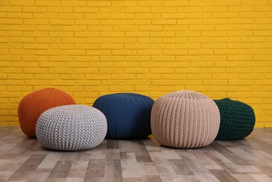Many different stylish poufs on floor near yellow brick wall in room
