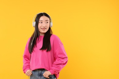 Portrait of smiling woman in headphones on orange background. Space for text