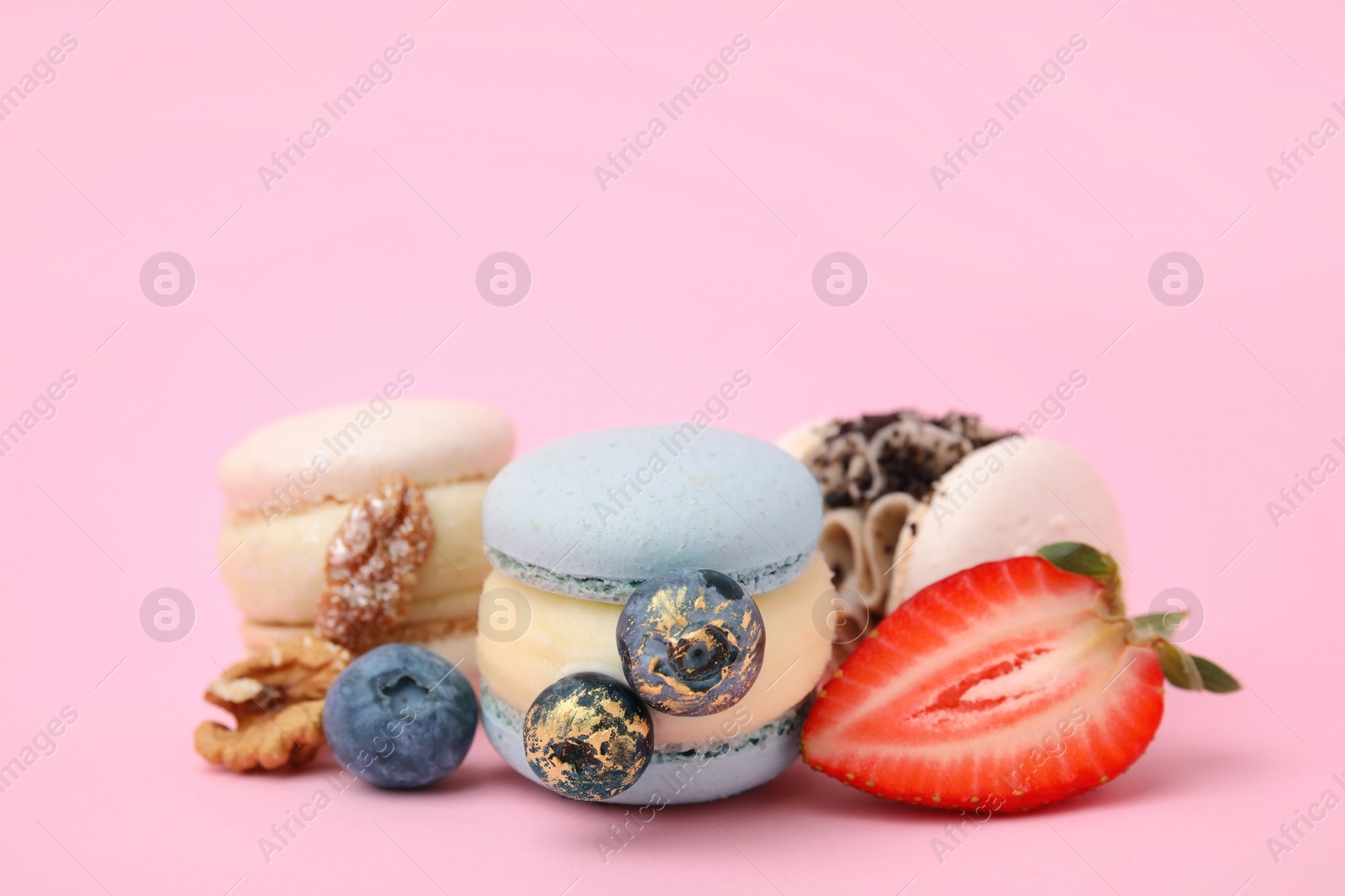 Photo of Delicious sweet macarons, berries and walnuts on pink background, closeup