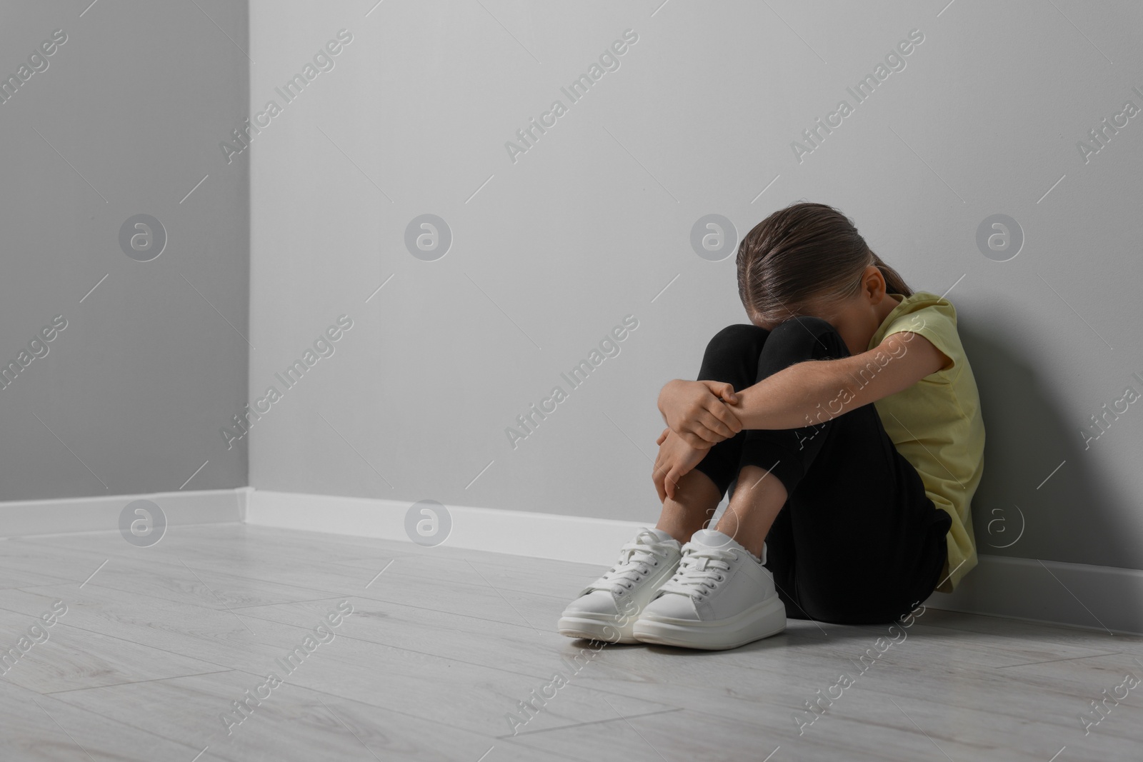 Photo of Child abuse. Upset girl sitting on floor near grey wall, space for text