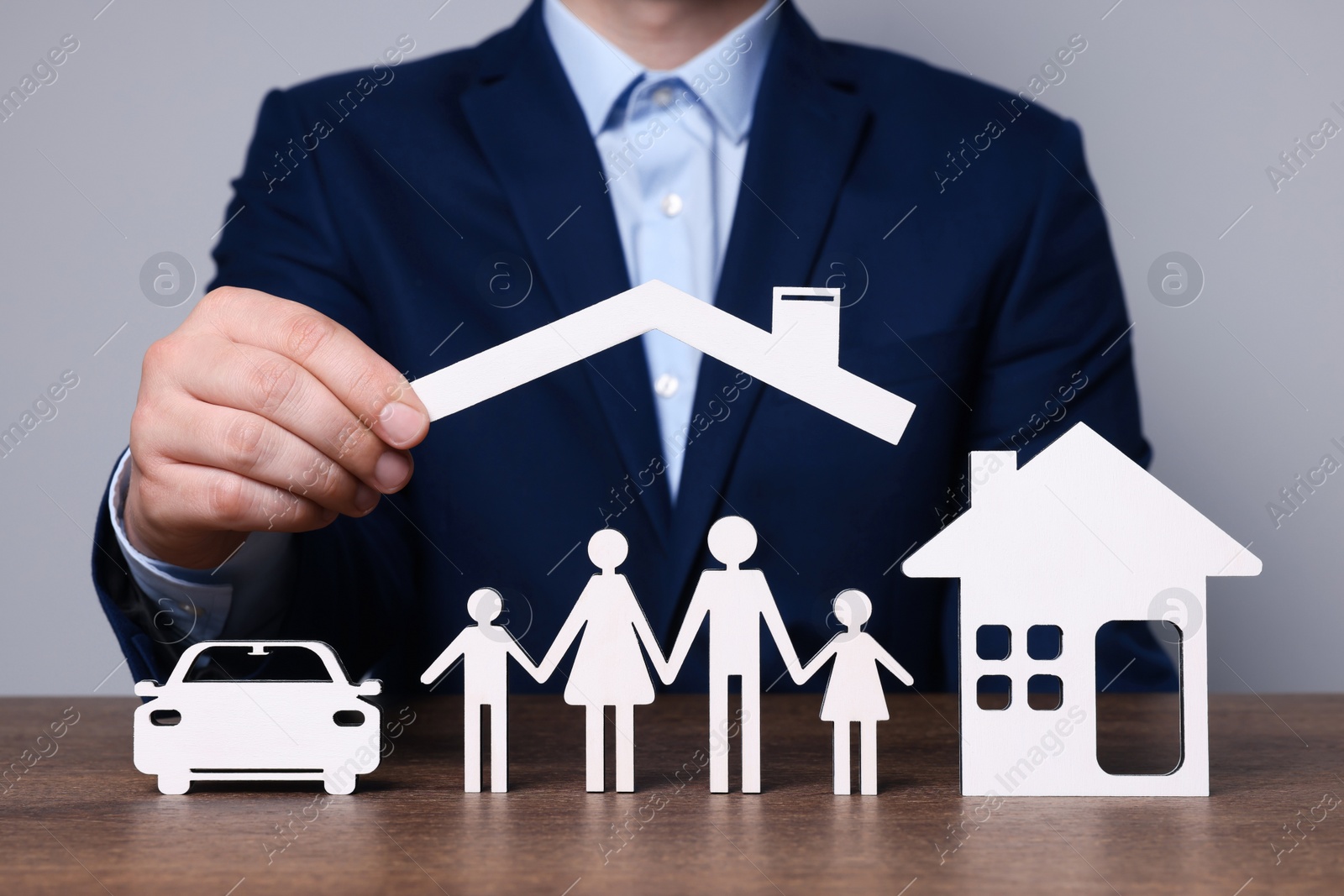 Photo of Man holding figure of roof above family at wooden table. closeup. Insurance concept