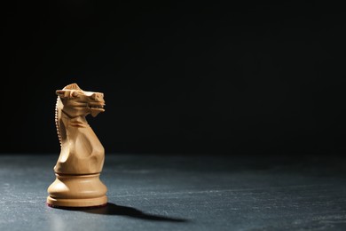Photo of Wooden knight on black table against dark background, space for text. Chess piece