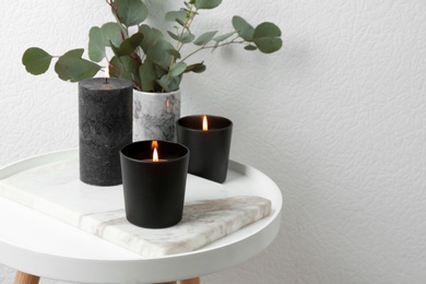 Photo of Burning candles and green branches on table at white wall, space for text