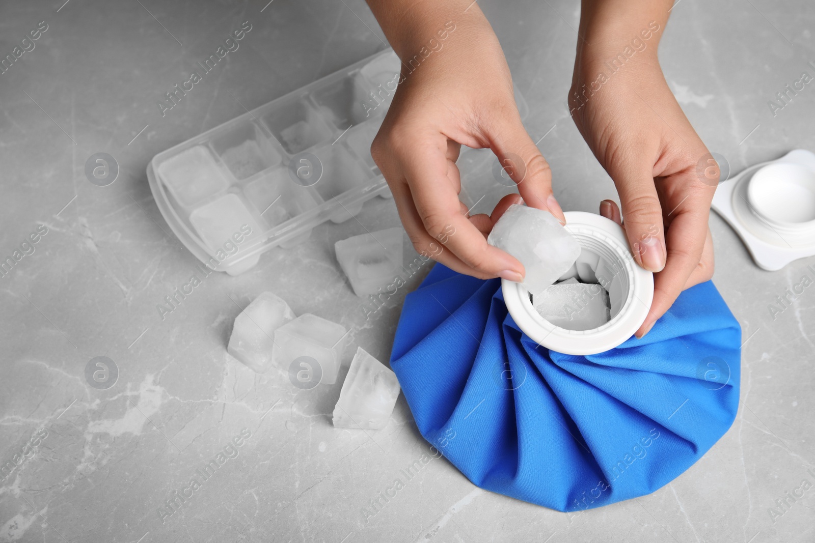 Photo of Woman putting ice cubes into pack at marble table, closeup