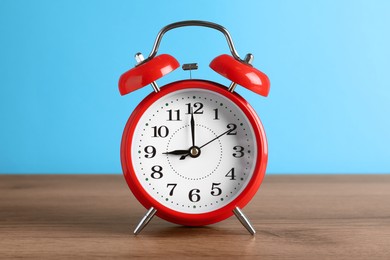 Red alarm clock on wooden table against light blue background