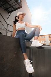 Photo of Smiling woman in sportswear sitting on parapet outdoors, low angle view