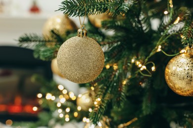Photo of Beautiful Christmas baubles hanging on fir tree branch in room, closeup
