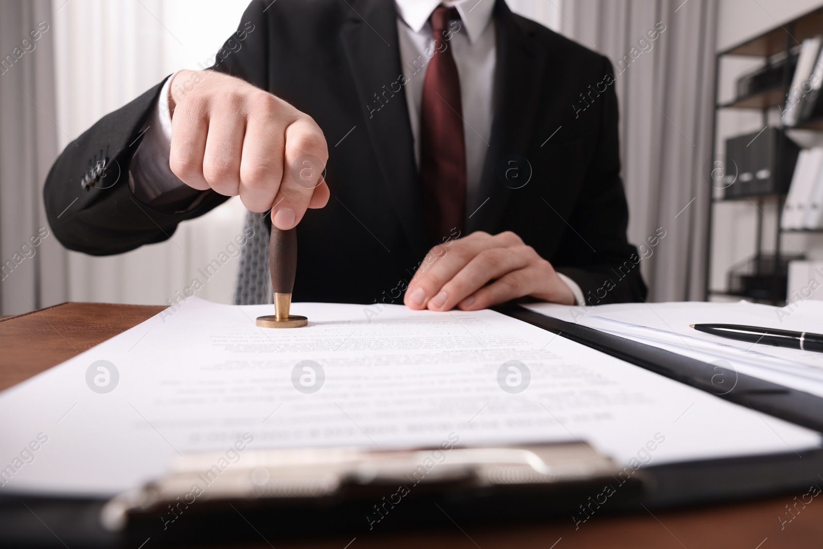 Photo of Notary stamping document at table in office, closeup