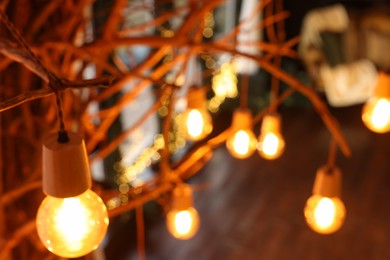 Photo of Dried tree branches beautifully decorated with light bulbs in room, blurred view