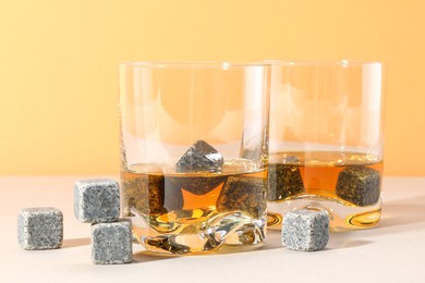 Whiskey stones and drink in glasses on light table, closeup