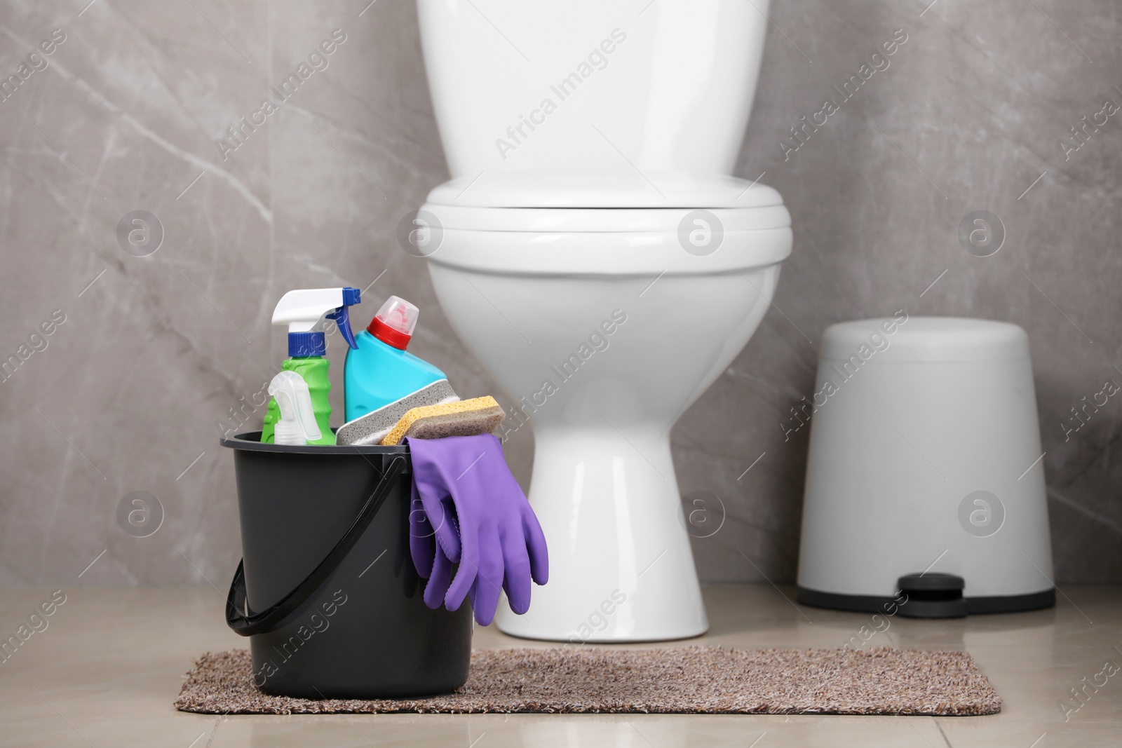 Photo of Bucket with cleaning supplies on floor in bathroom, space for text