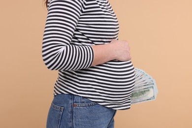 Surrogate mother. Pregnant woman with dollar banknotes on beige background, closeup