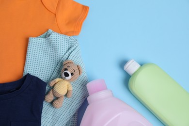 Bottles of laundry detergents, baby clothes and toy bear on light blue background, flat lay. Space for text