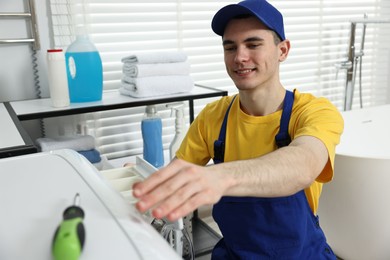 Smiling plumber repairing washing machine in bathroom