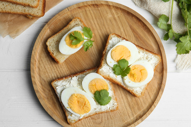 Photo of Tasty sandwiches with boiled eggs served on white wooden table, flat lay