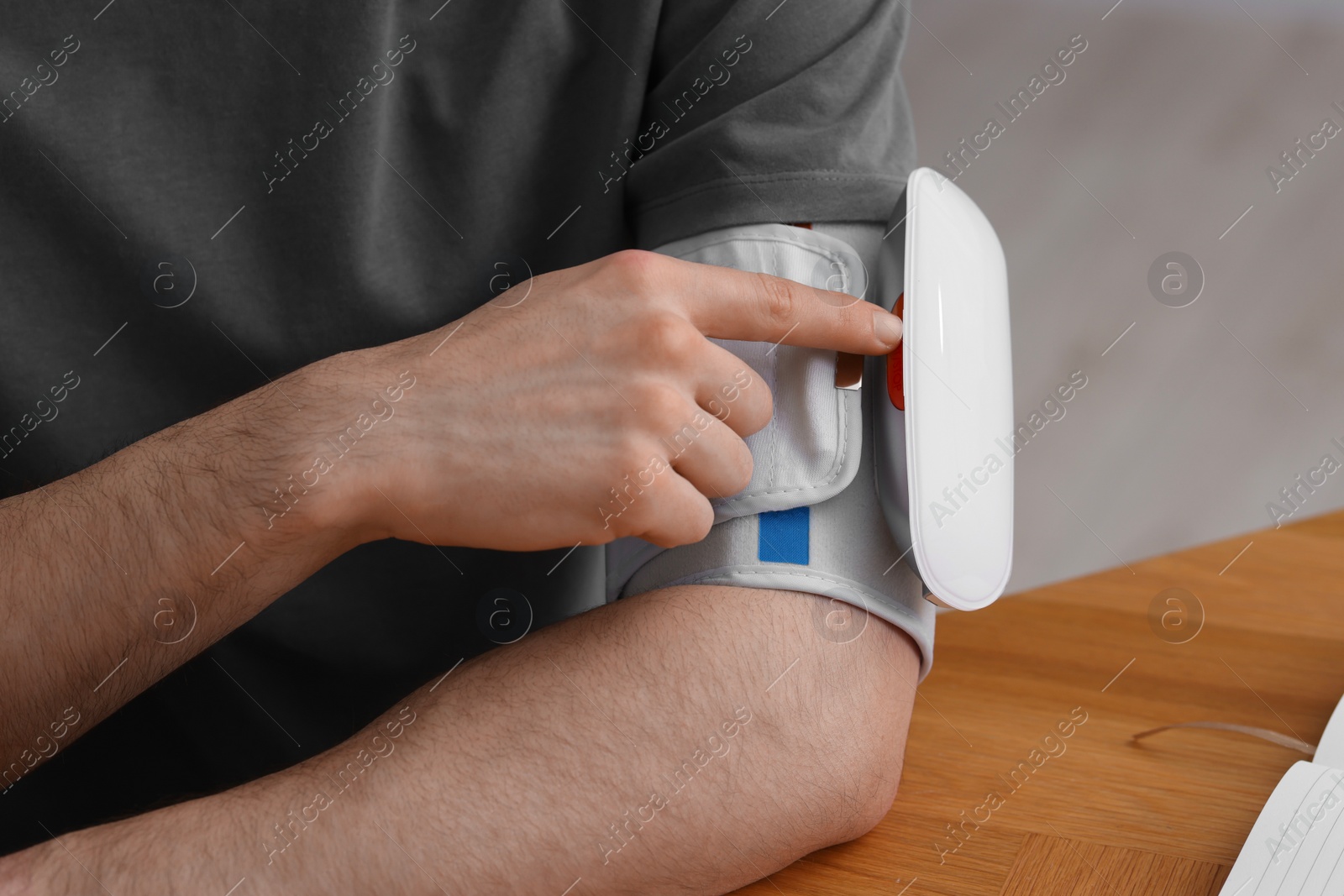 Photo of Man measuring his blood pressure with tonometer at wooden table indoors, closeup