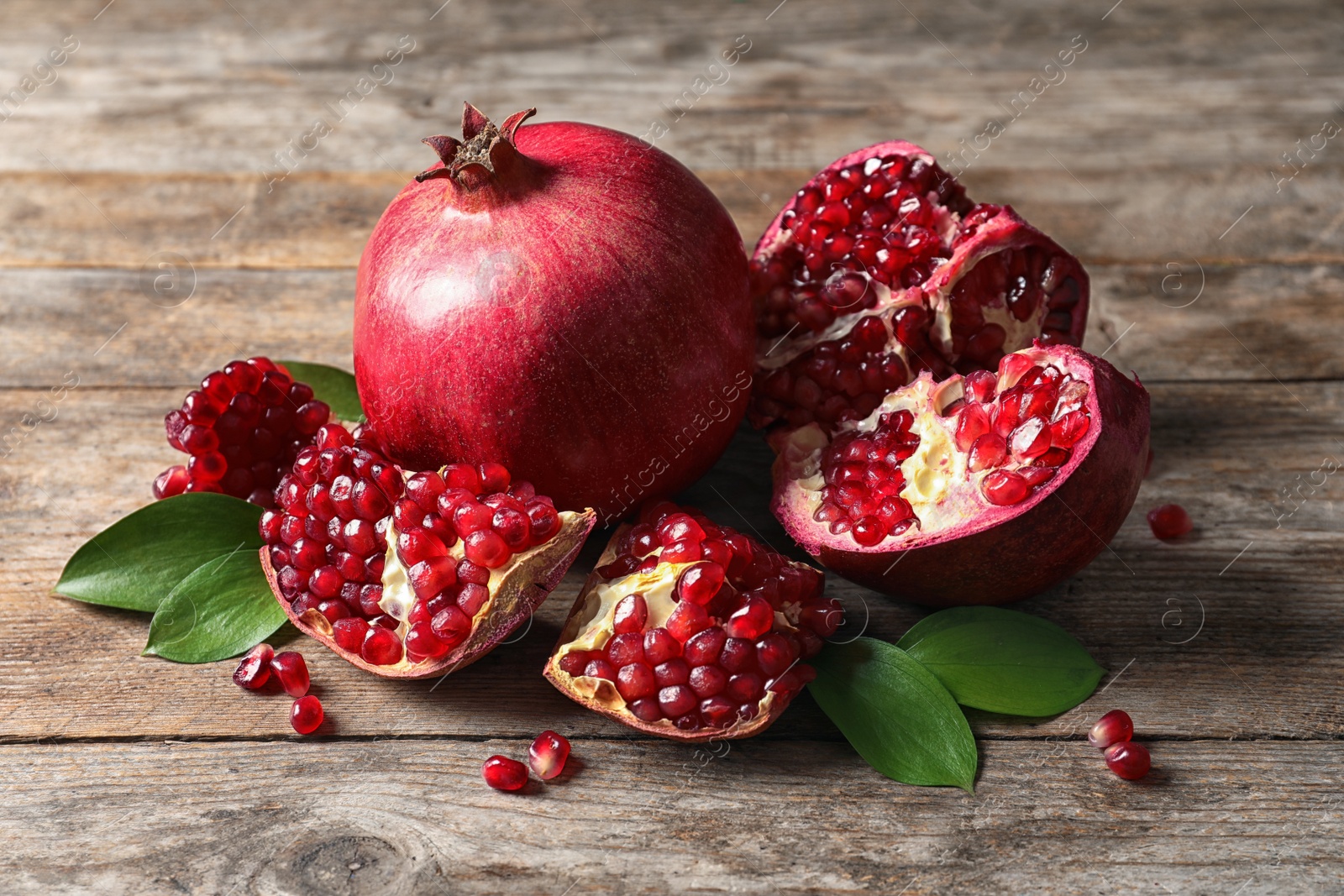 Photo of Ripe pomegranates and leaves on wooden background