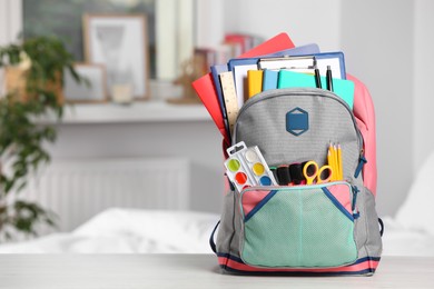 Photo of Backpack with different school stationery on white table indoors, space for text
