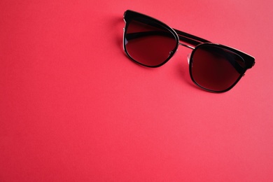 Photo of Stylish sunglasses on pink background, top view. Space for text