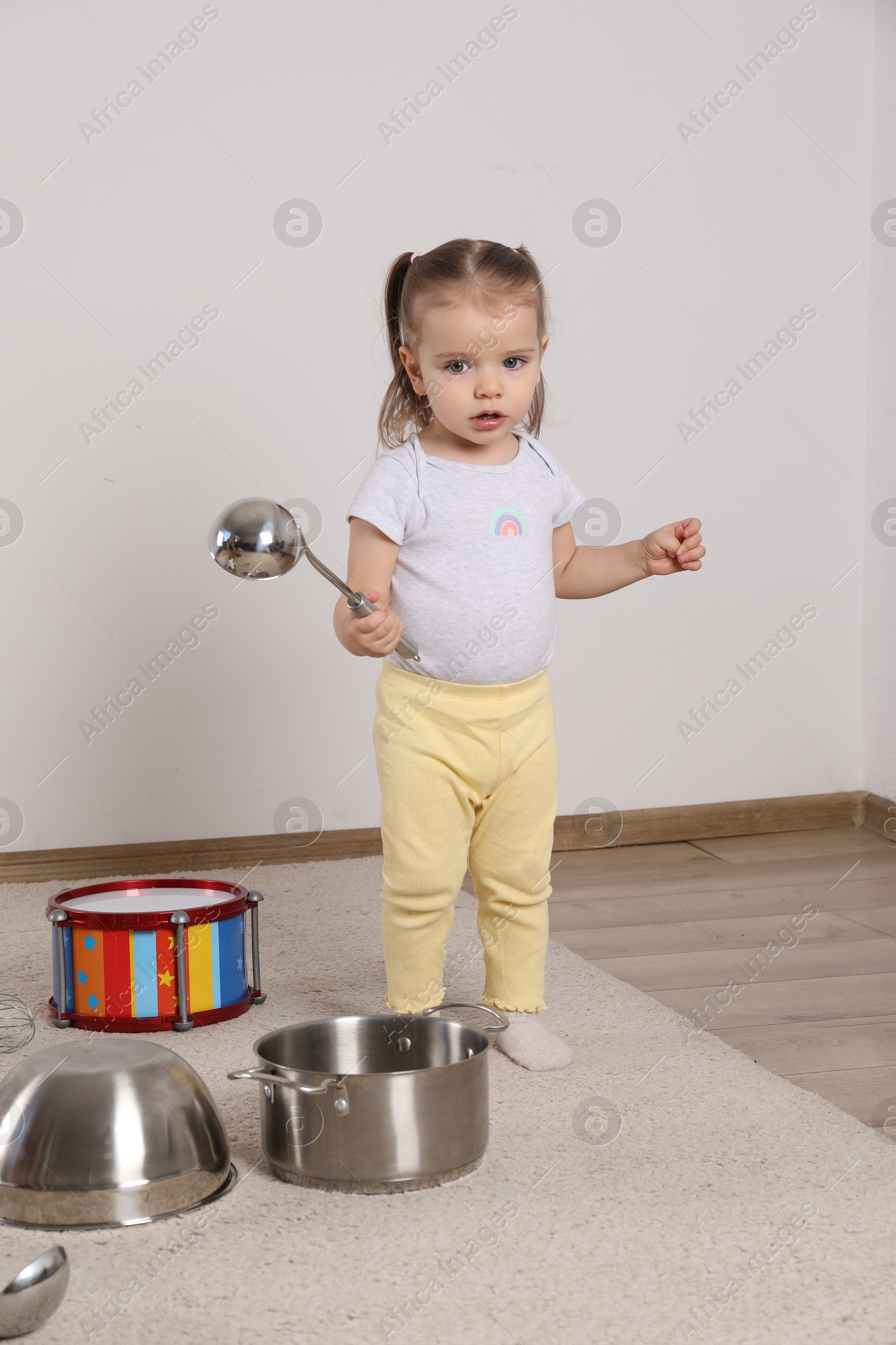 Photo of Cute little girl with cookware and toy drum at home