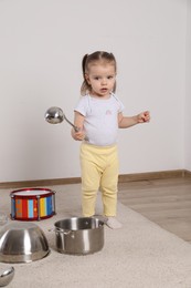 Cute little girl with cookware and toy drum at home