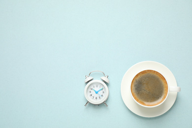 Cup of morning coffee and alarm clock on light background, flat lay. Space for text