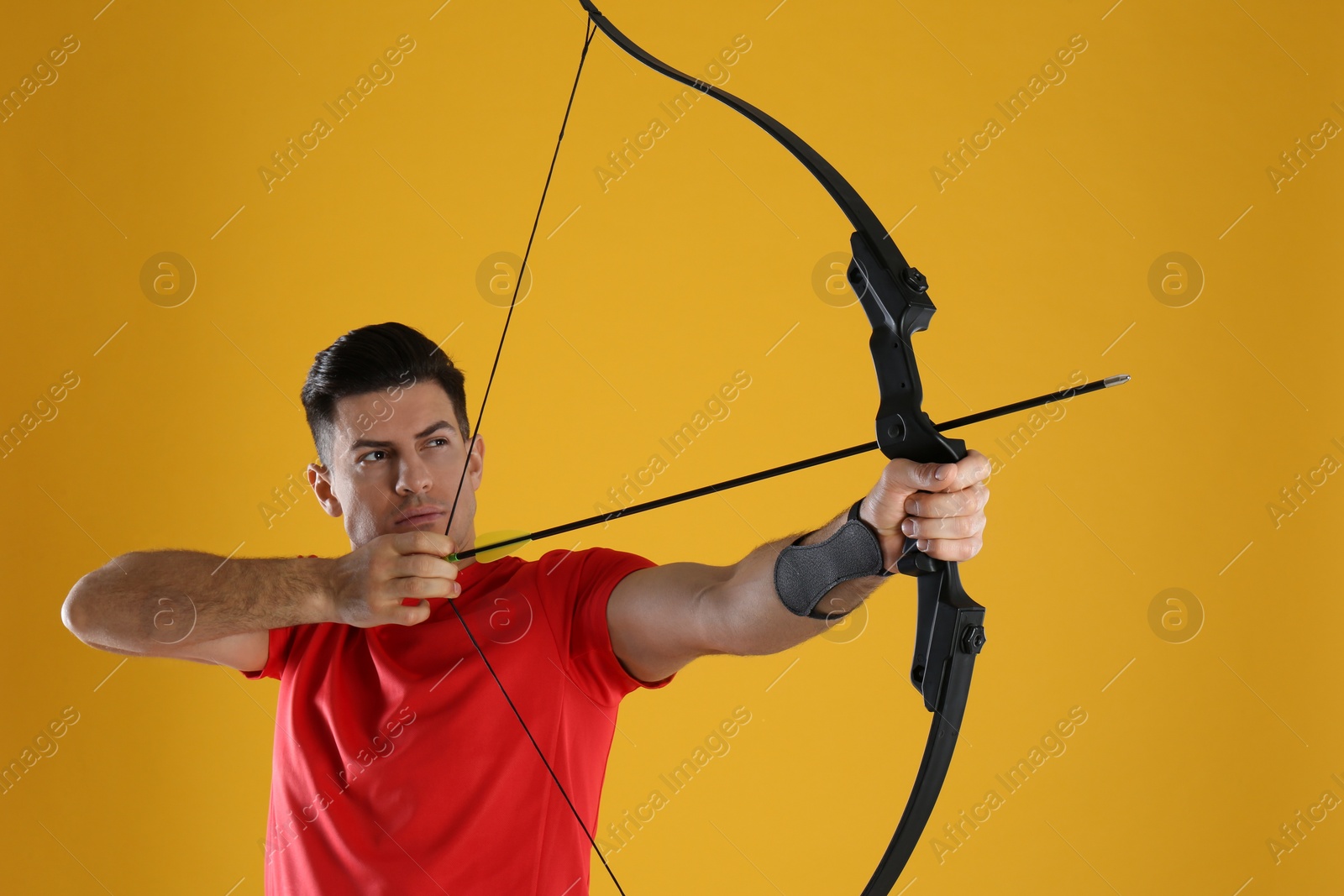 Photo of Man with bow and arrow practicing archery on yellow background