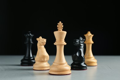 Photo of Different chess pieces on grey table against dark background