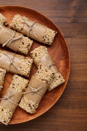 Photo of Plate with tasty sesame seed bars on wooden table, top view