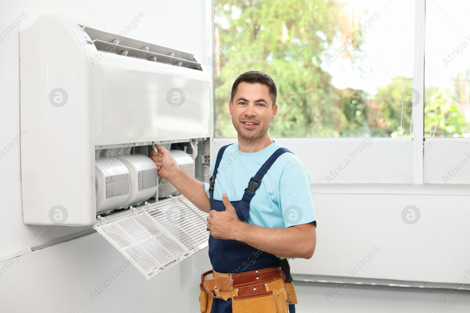 Photo of Male technician standing near air conditioner indoors
