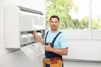 Photo of Male technician standing near air conditioner indoors