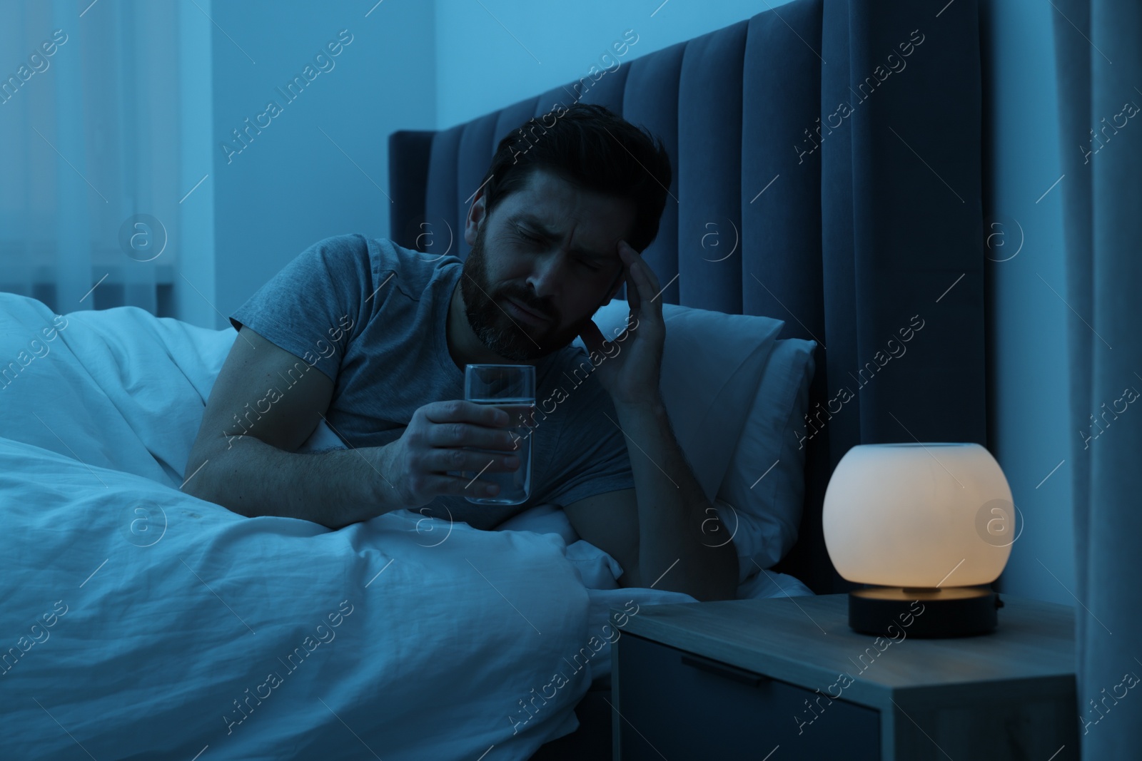 Photo of Man with glass of water suffering from headache in bed at night