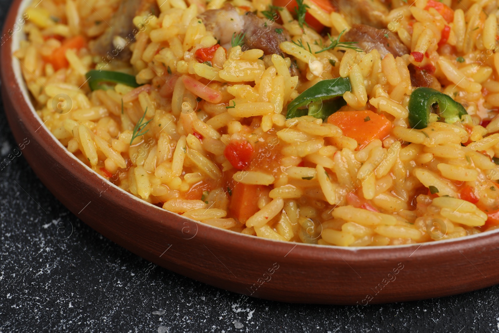 Photo of Delicious pilaf with meat on black textured table, closeup