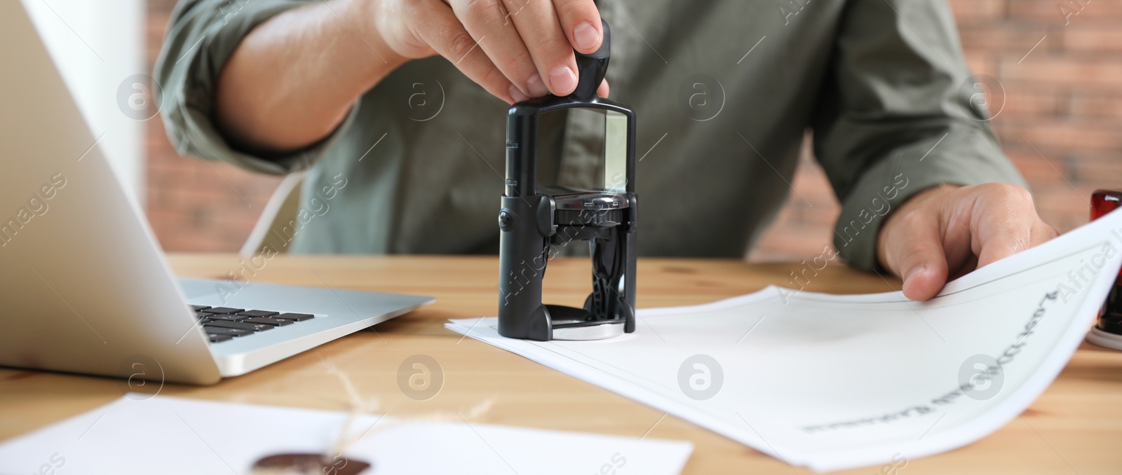 Image of Male notary stamping document at table in office, closeup. Banner design