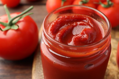 Jar of tasty ketchup and tomatoes on wooden table, closeup