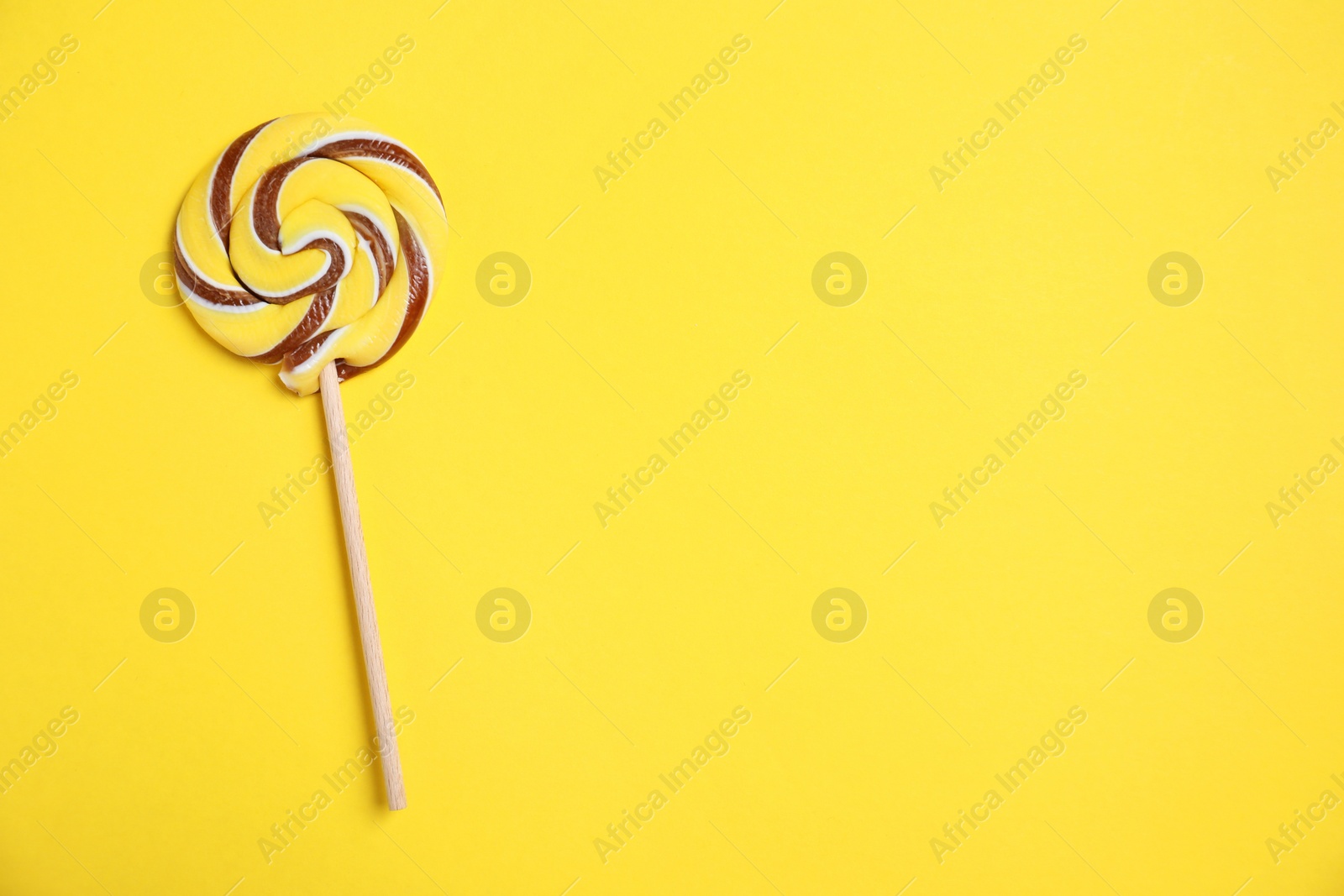 Photo of Stick with colorful lollipop swirl on yellow background, top view. Space for text