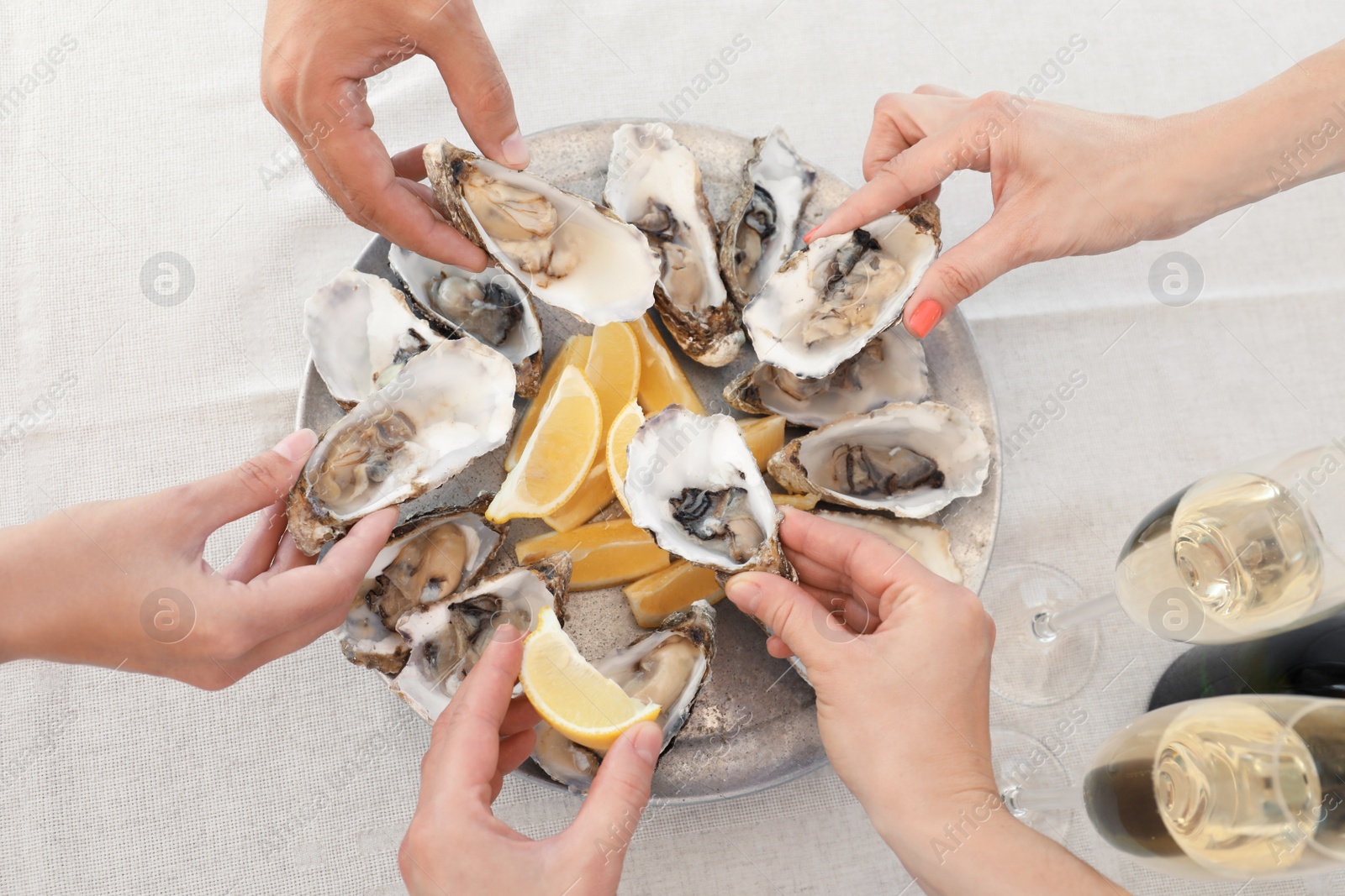 Photo of Top view of people with fresh oysters at table, focus on hands